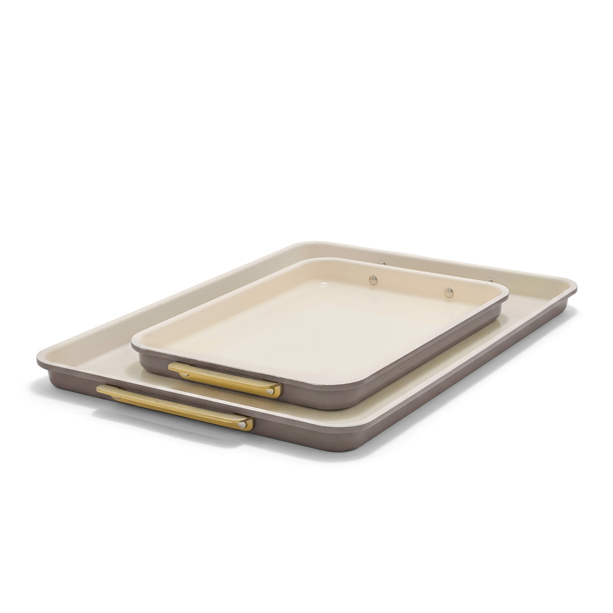 Reserve Bakeware 2-piece sheet pan set in latte, featuring two light tan and taupe nesting pans with gold-toned metal handles.