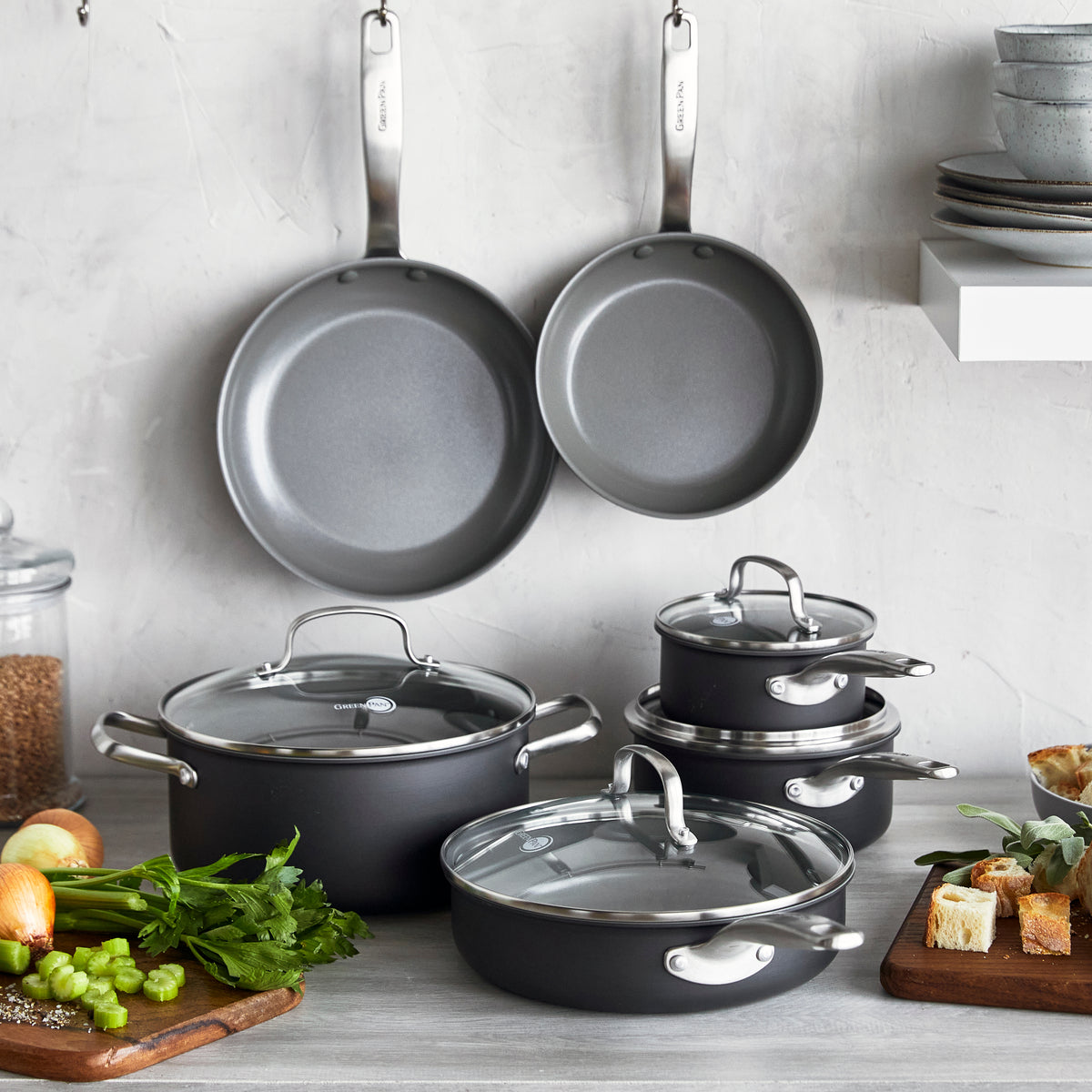 Chatham ceramic nonstick 10-piece cookware set with glass lids hanging above counter, surrounded by vegetables and bread.