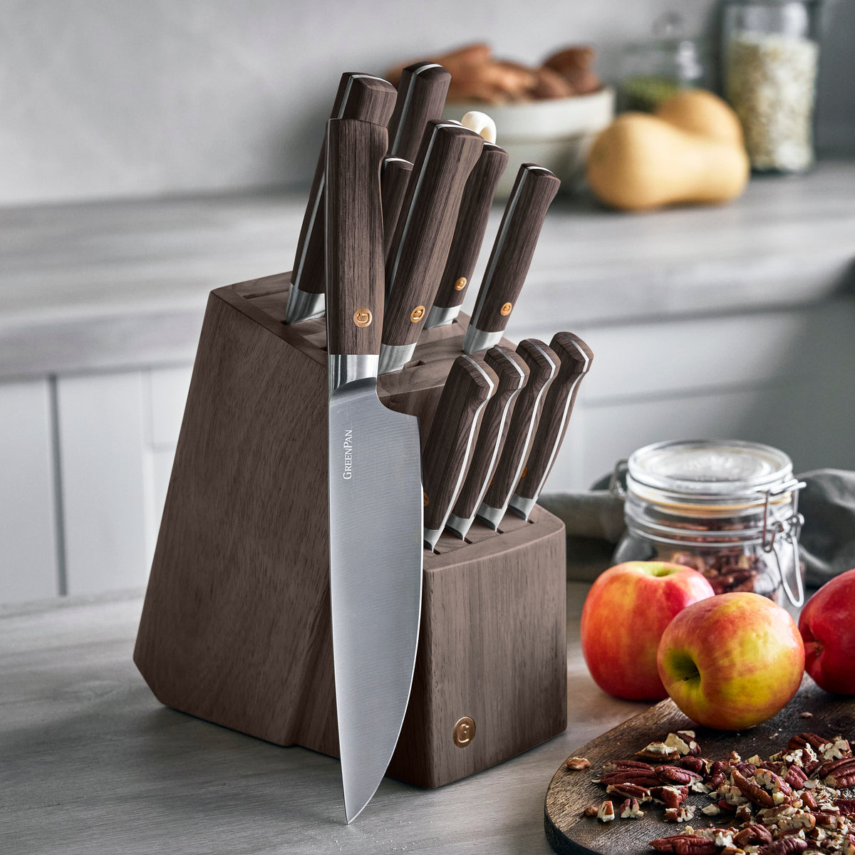 13-piece knife block set with dark wood handles on a kitchen counter near apples, nuts, and jars.