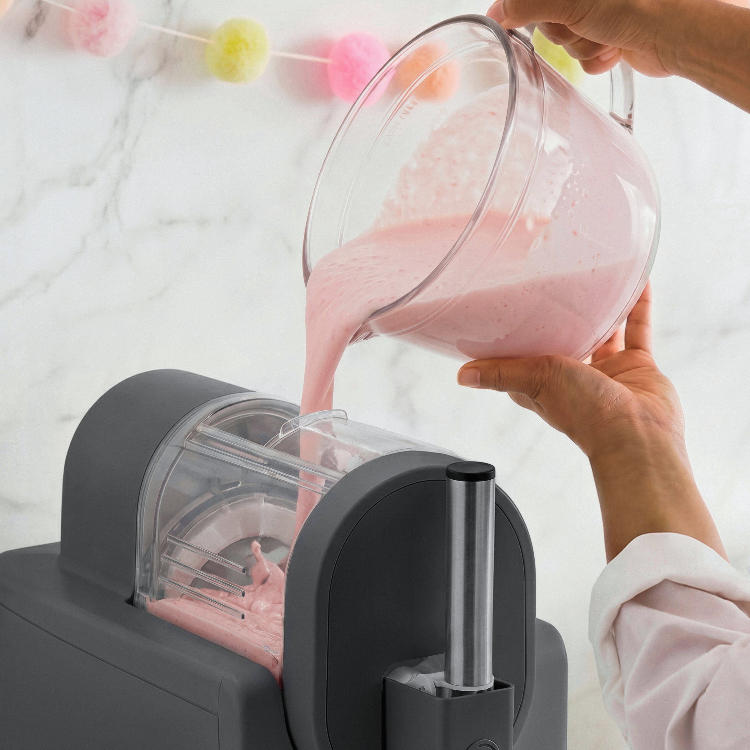 Person pouring pink liquid from a glass pitcher into an ice cream maker
