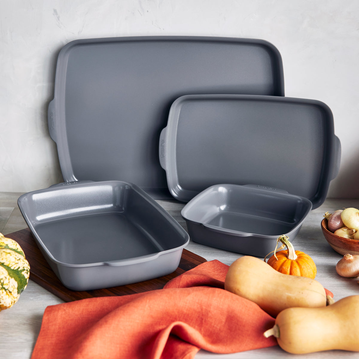 Gray ceramic nonstick 4-piece ovenware set on a counter with squash, pumpkins, potatoes, and an orange cloth nearby.