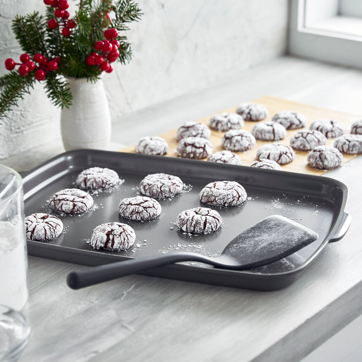 Baking tray with cookies and a spatula on a kitchen counter with Christmas decorations.