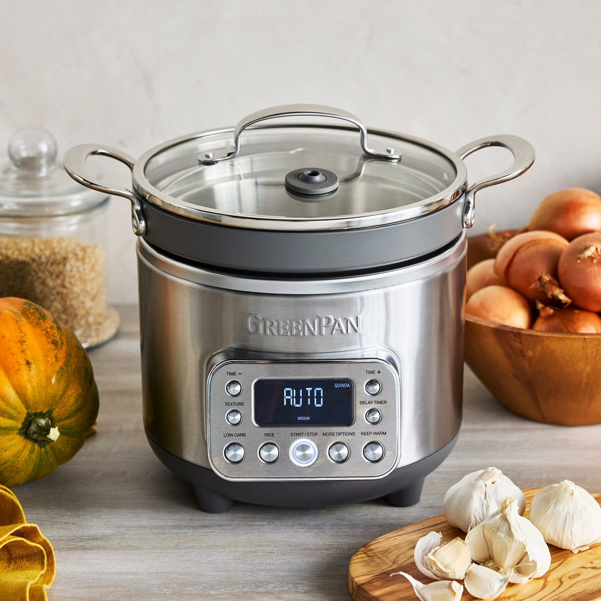 Rice and grains cooker on counter with onions, garlic, pumpkin, and a jar of rice.