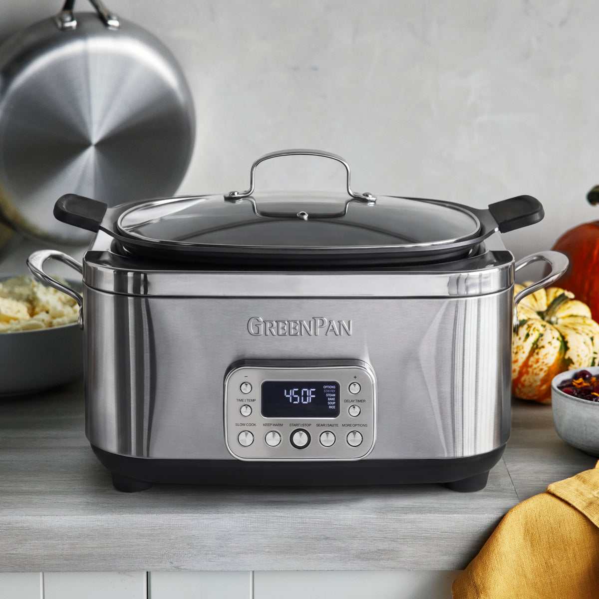 Stainless steel 6-quart slow cooker on a kitchen counter next to pumpkins and a bowl of mashed potatoes.