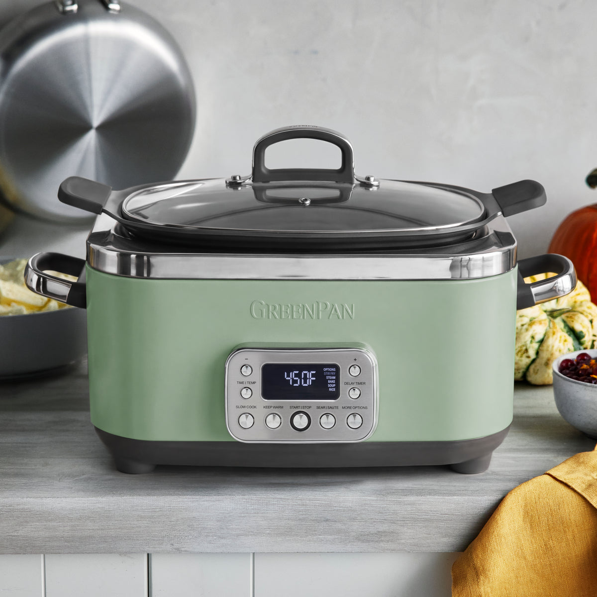 Sage 6-quart slow cooker with buttons sits on a counter next to vegetables and a yellow cloth.