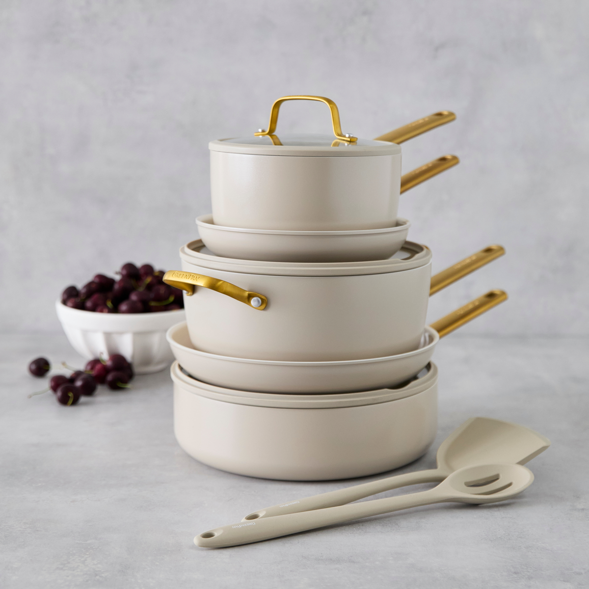 Stack of taupe cookware with gold handles on a gray background