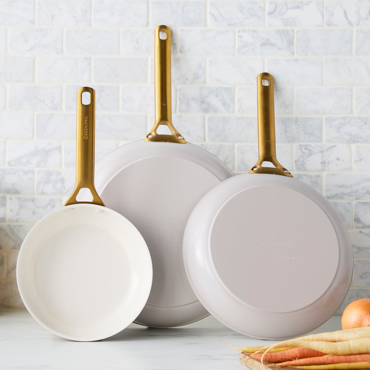 Three taupe gray frying pans with gold handles on a kitchen counter