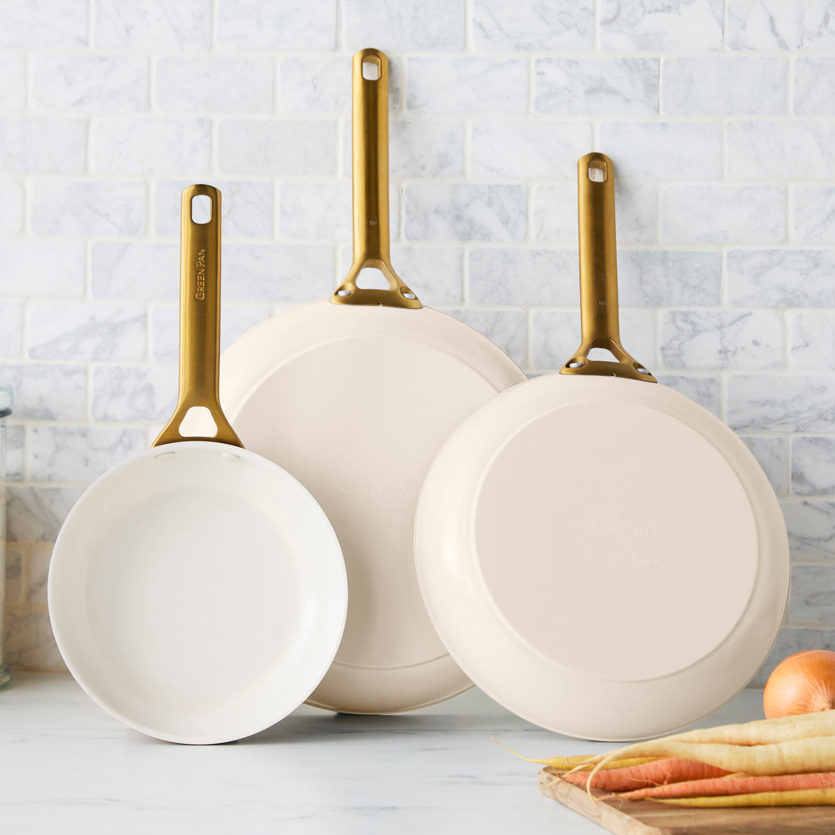 Three taupe frying pans with gold handles on a kitchen counter