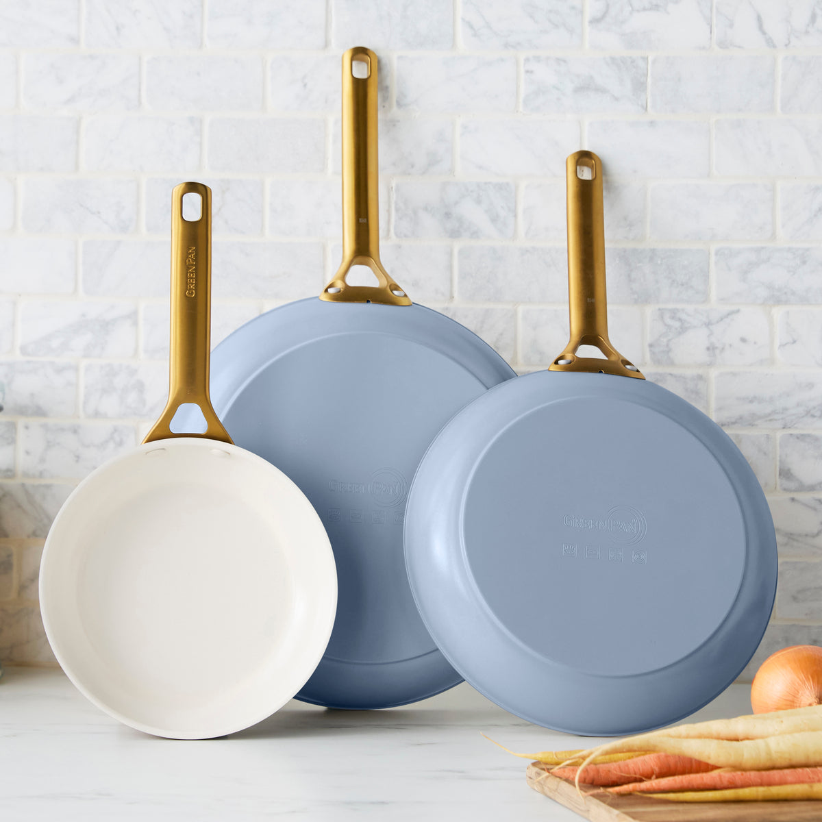 Three blue frying pans with gold handles on a kitchen counter