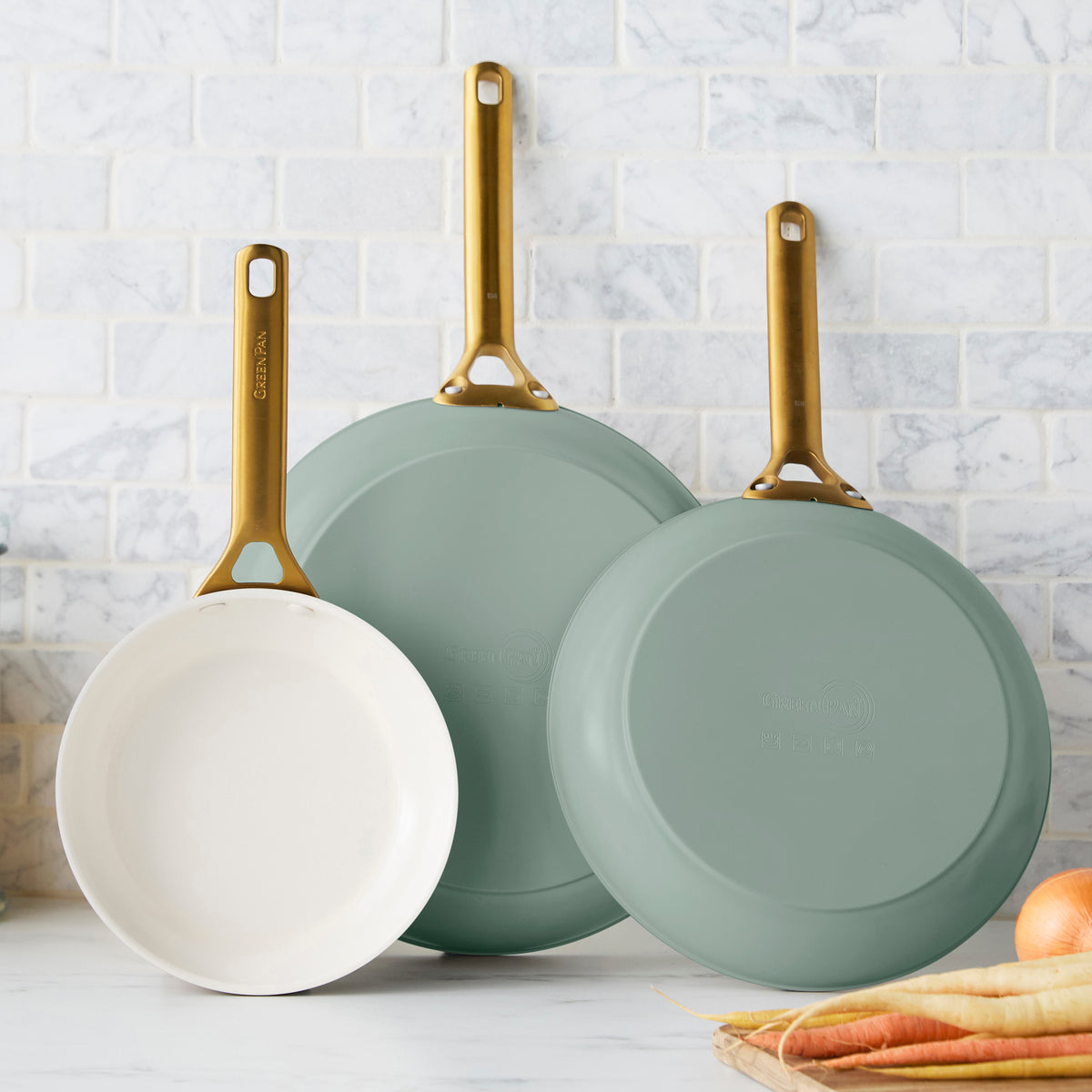 Three green frying pans on a kitchen counter with a tiled wall background.