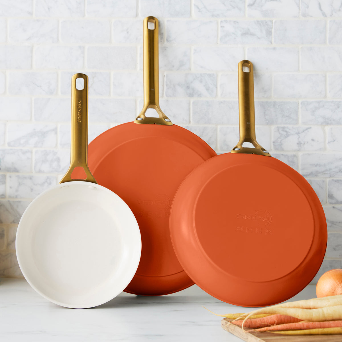 Three dark orange frying pans on a kitchen counter with a tiled wall background.