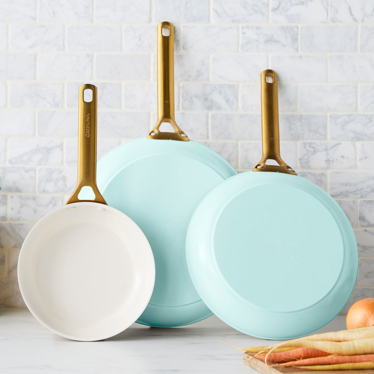 Three light blue frying pans with gold handles on a kitchen counter.