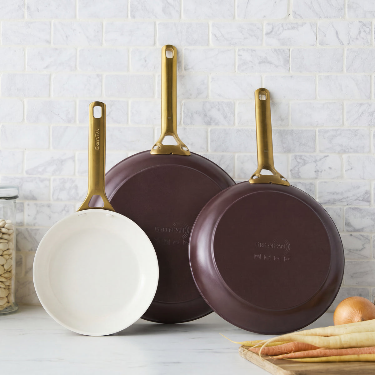 Set of three Bordeaux ceramic frypans stacked on a counter with beans, onions, and carrots nearby.