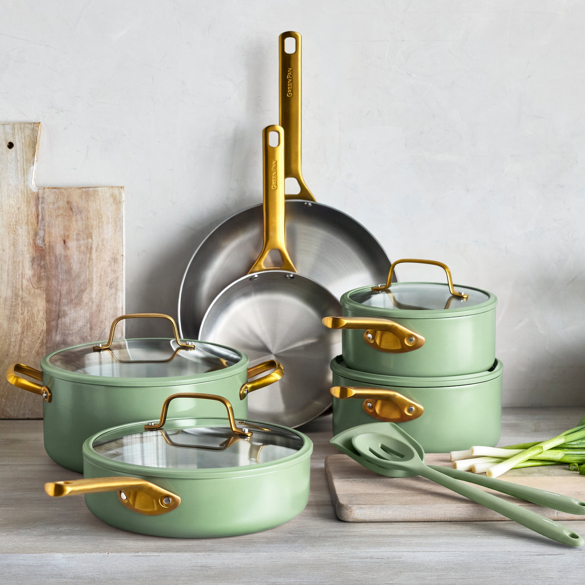 Sage green stainless steel 12-piece cookware set on a counter with spring onions and kitchen utensils beside it.