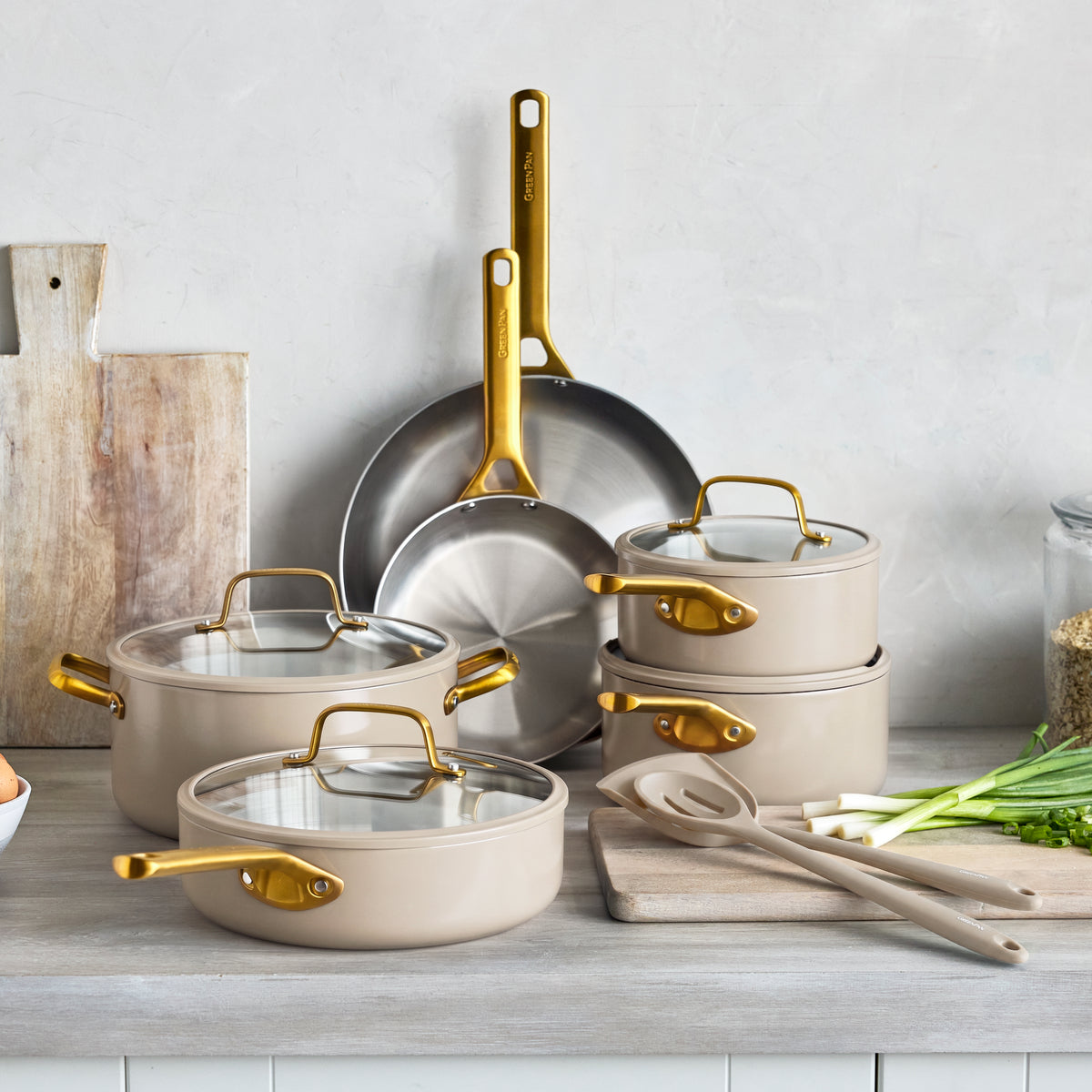 12-piece uncoated stainless steel cookware set in macadamia on a kitchen counter near wooden cutting boards.