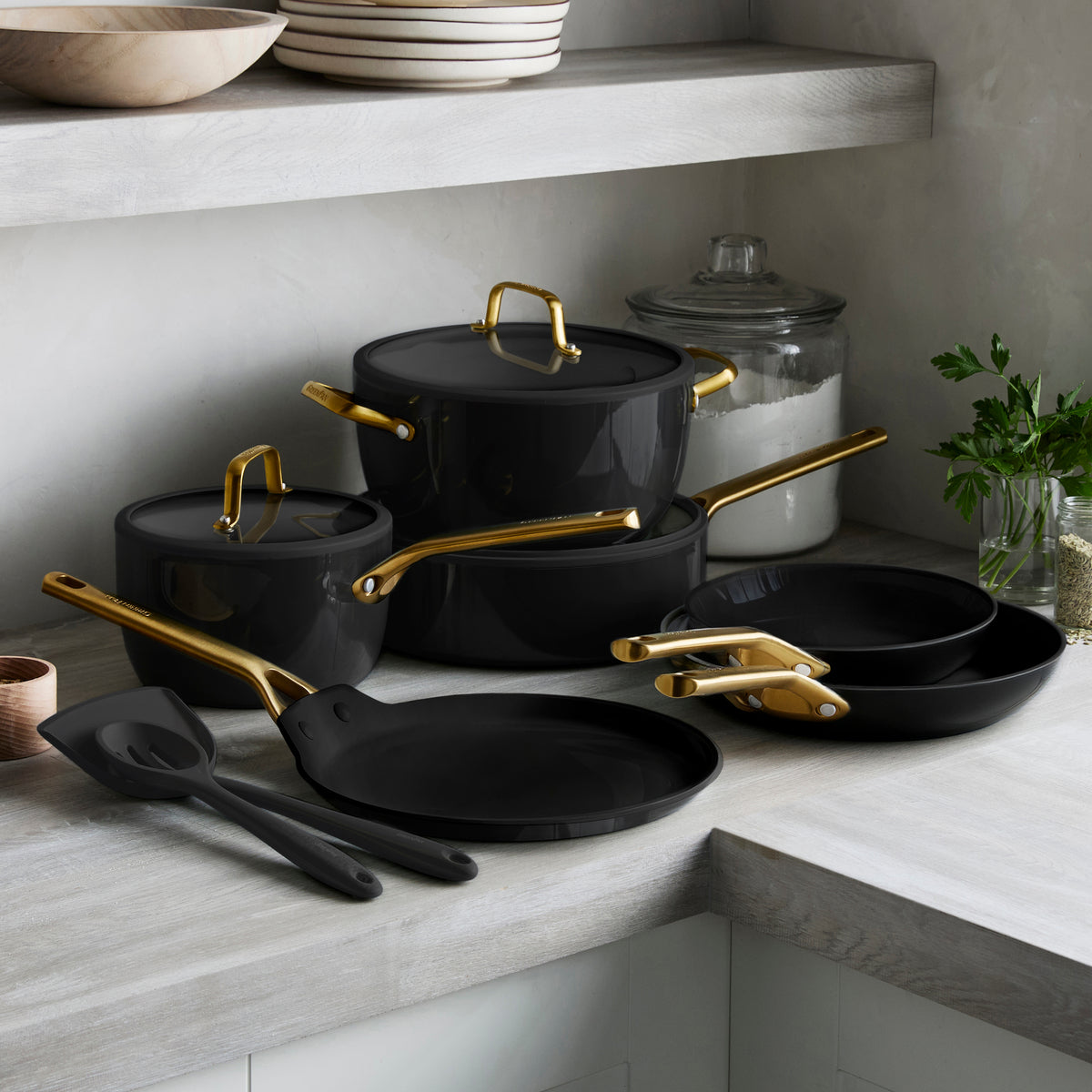 Set of black cookware with gold handles on a kitchen counter.