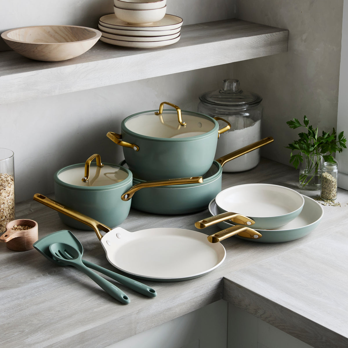 Set of green cookware with gold handles on a kitchen counter.
