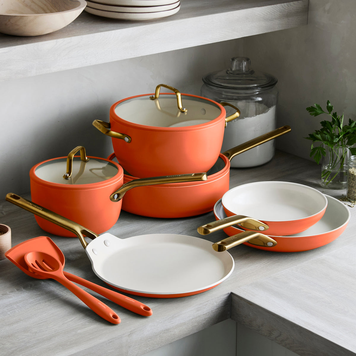 Set of orange cookware with gold handles on a kitchen counter.