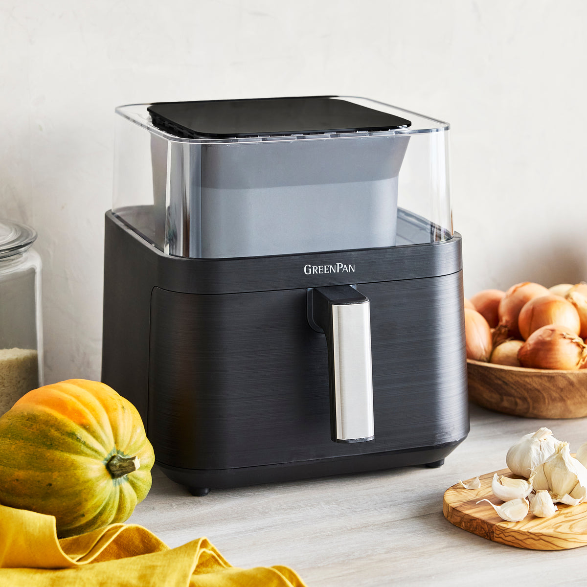 Clear view air fryer on a kitchen counter next to garlic, onions, and squash.
