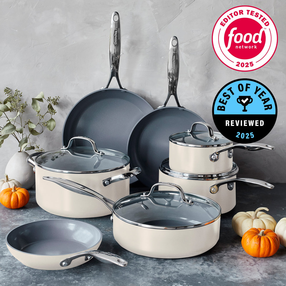Cream ceramic 11-piece cookware set with glass lids on a gray counter, pumpkins visible in the background.