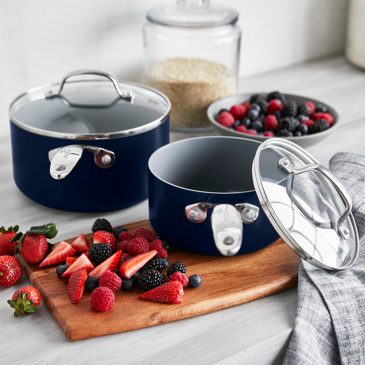 Two Valencia Pro Twilight saucepans with lids on a kitchen counter next to a cutting board of fresh berries.