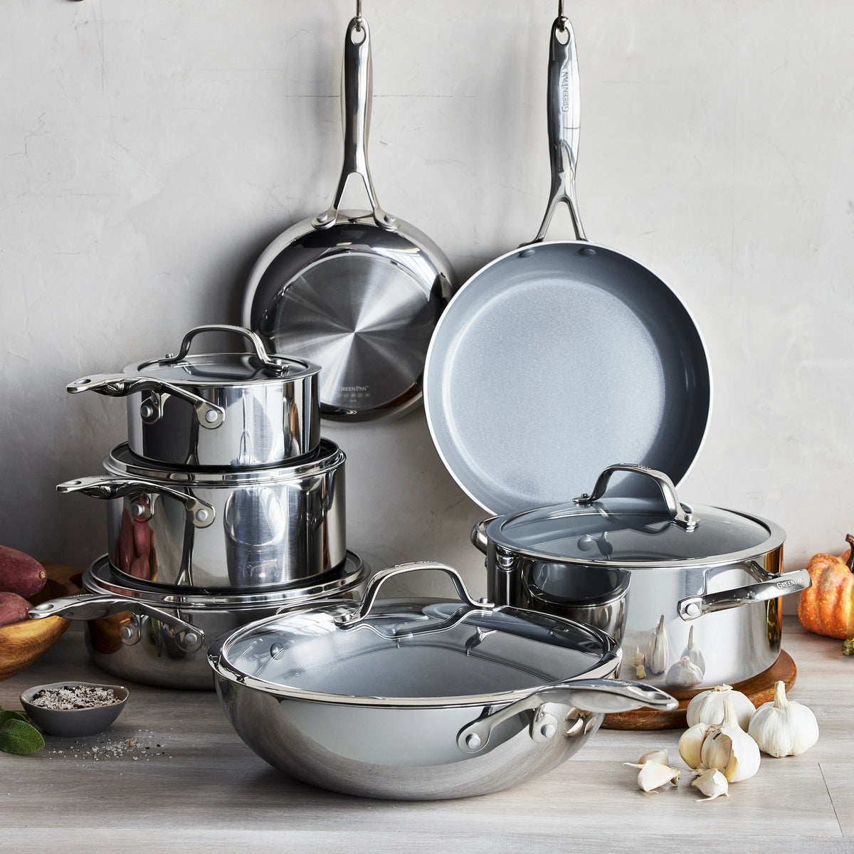 Stainless steel 10-piece cookware set with lids, arranged on a wooden surface near garlic and assorted vegetables.