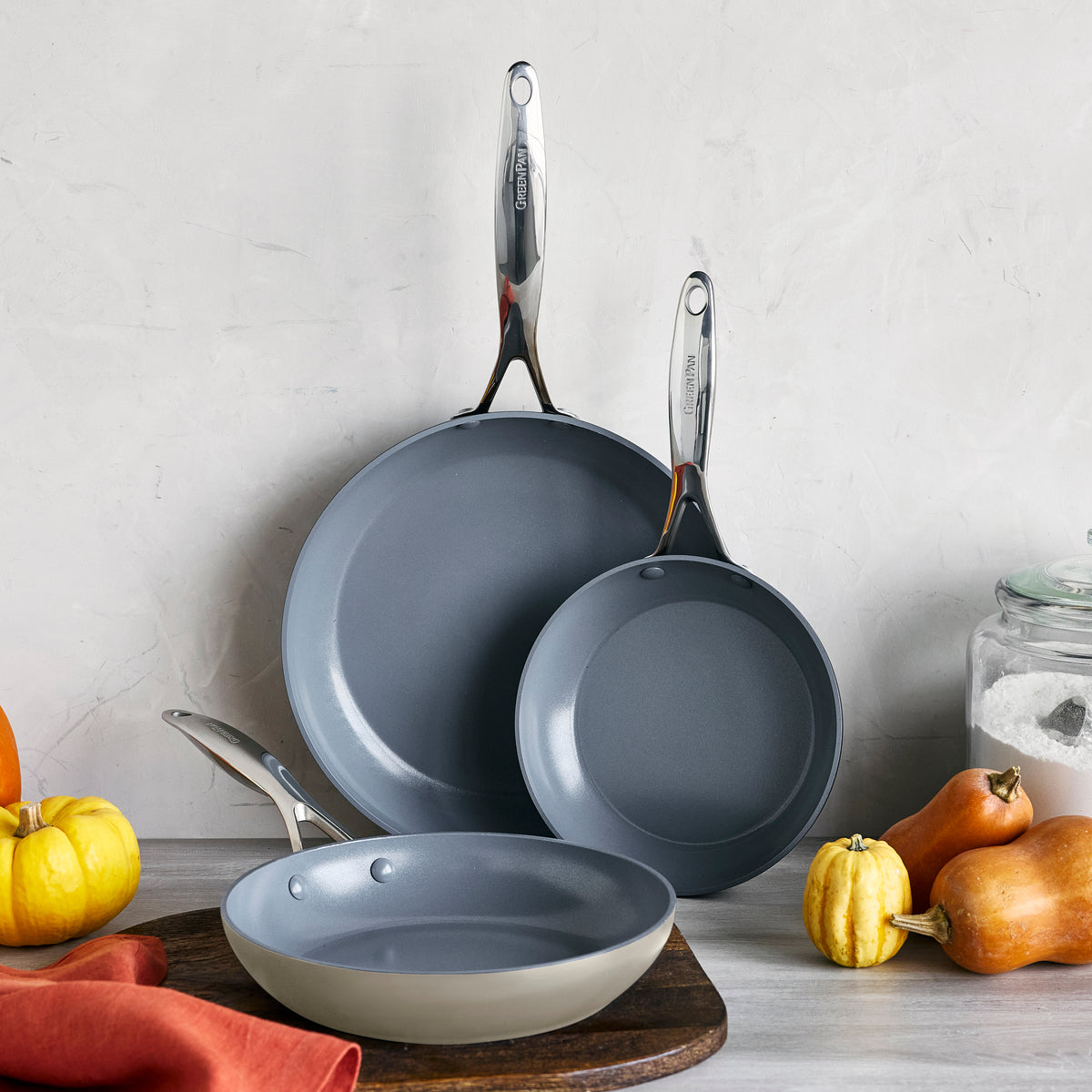 Three ceramic nonstick frypans in different sizes on a counter with pumpkins, salt, and an orange cloth.