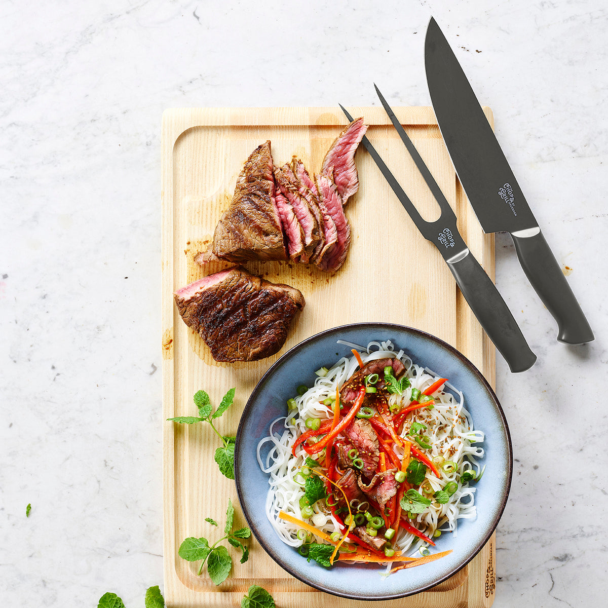 Steak and noodle salad next to the Chop  Grill 2-piece knife set with wooden handles on a wooden board.