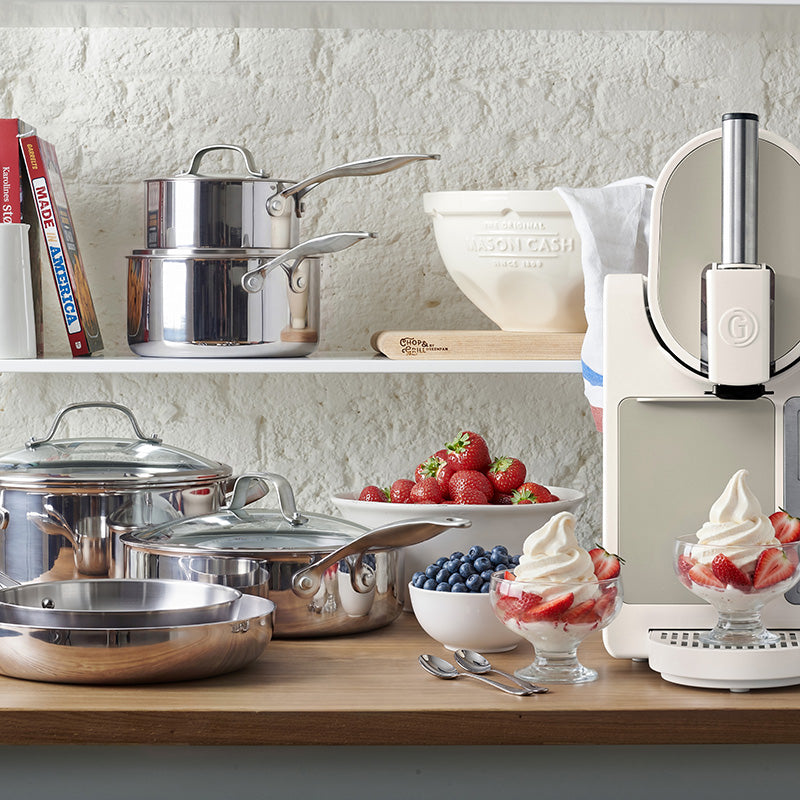 Stainless steel cookware, a GreenPan skillet, mixing bowl, and bowls of berries on a kitchen counter with parfaits.