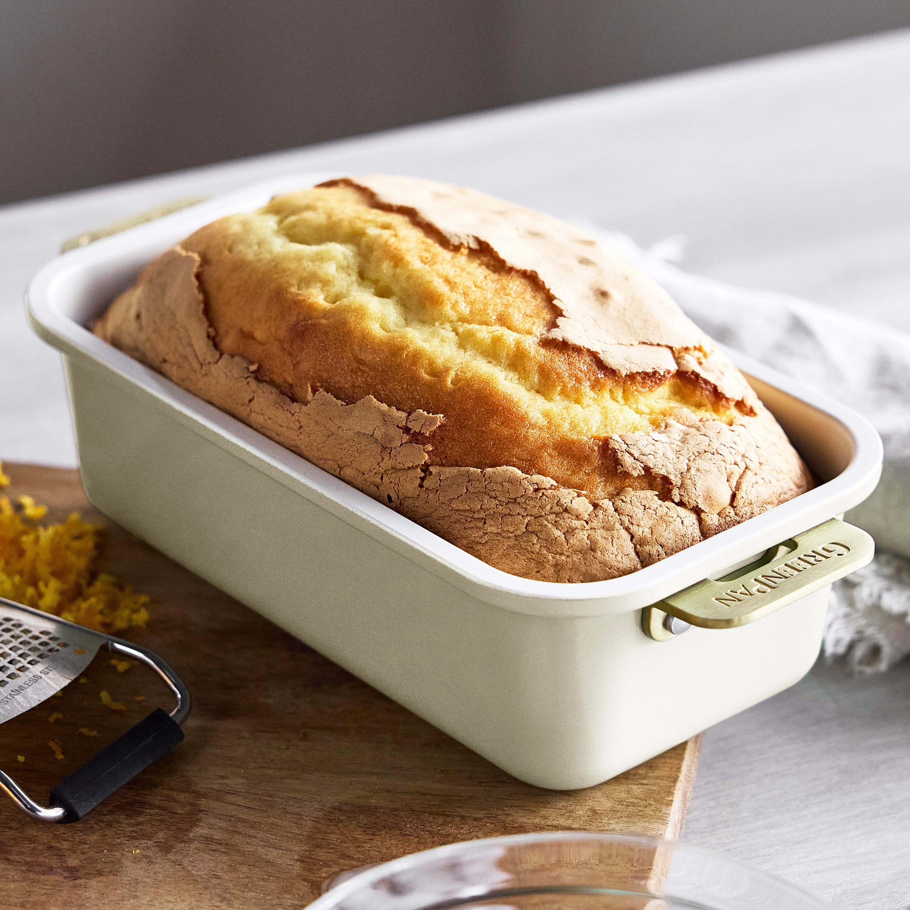 Loaf of cake in a cream loaf pan on a wooden cutting board with a grater.