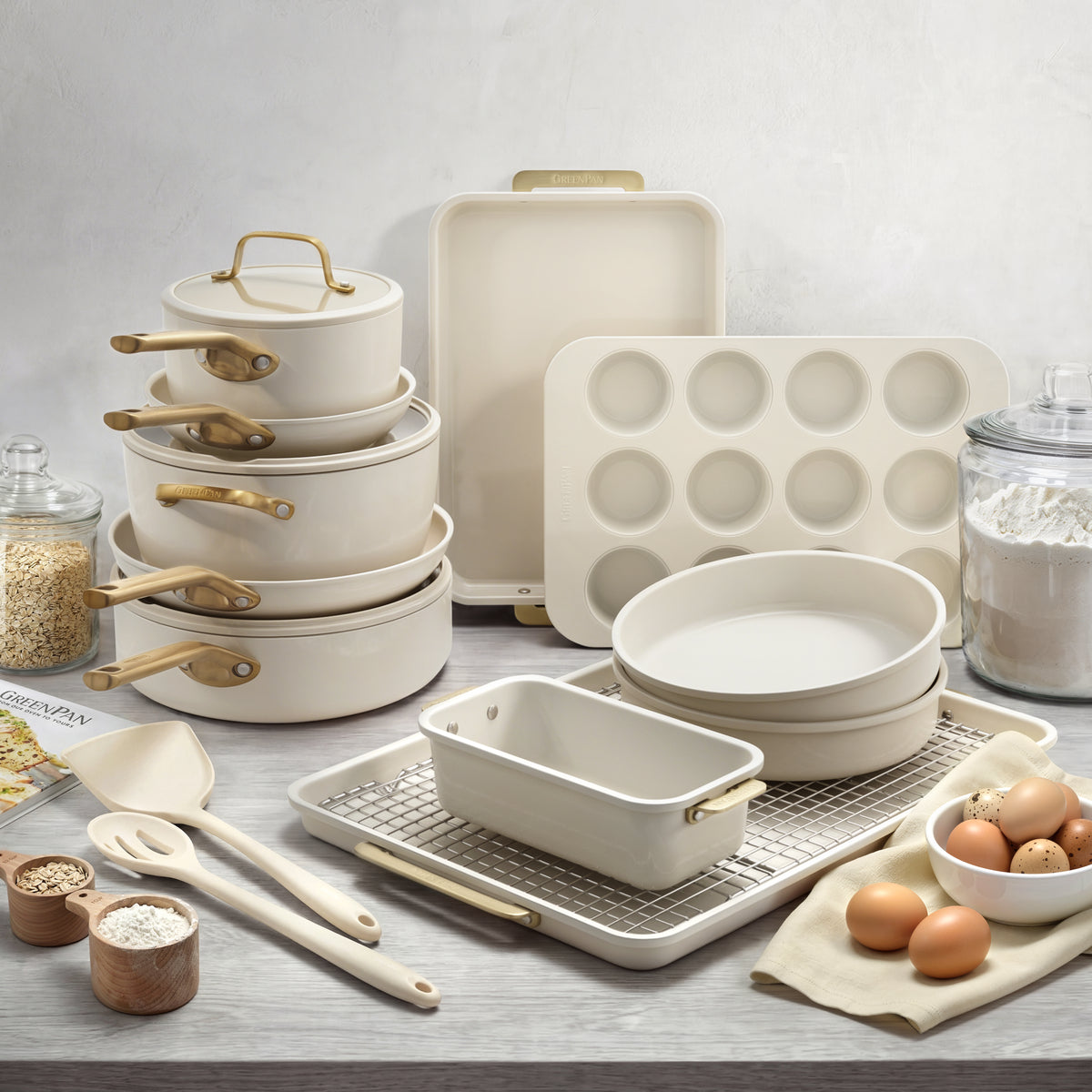 Cream cookware and bakeware set with gold handles, 18 pieces, arranged on a kitchen counter with baking ingredients.