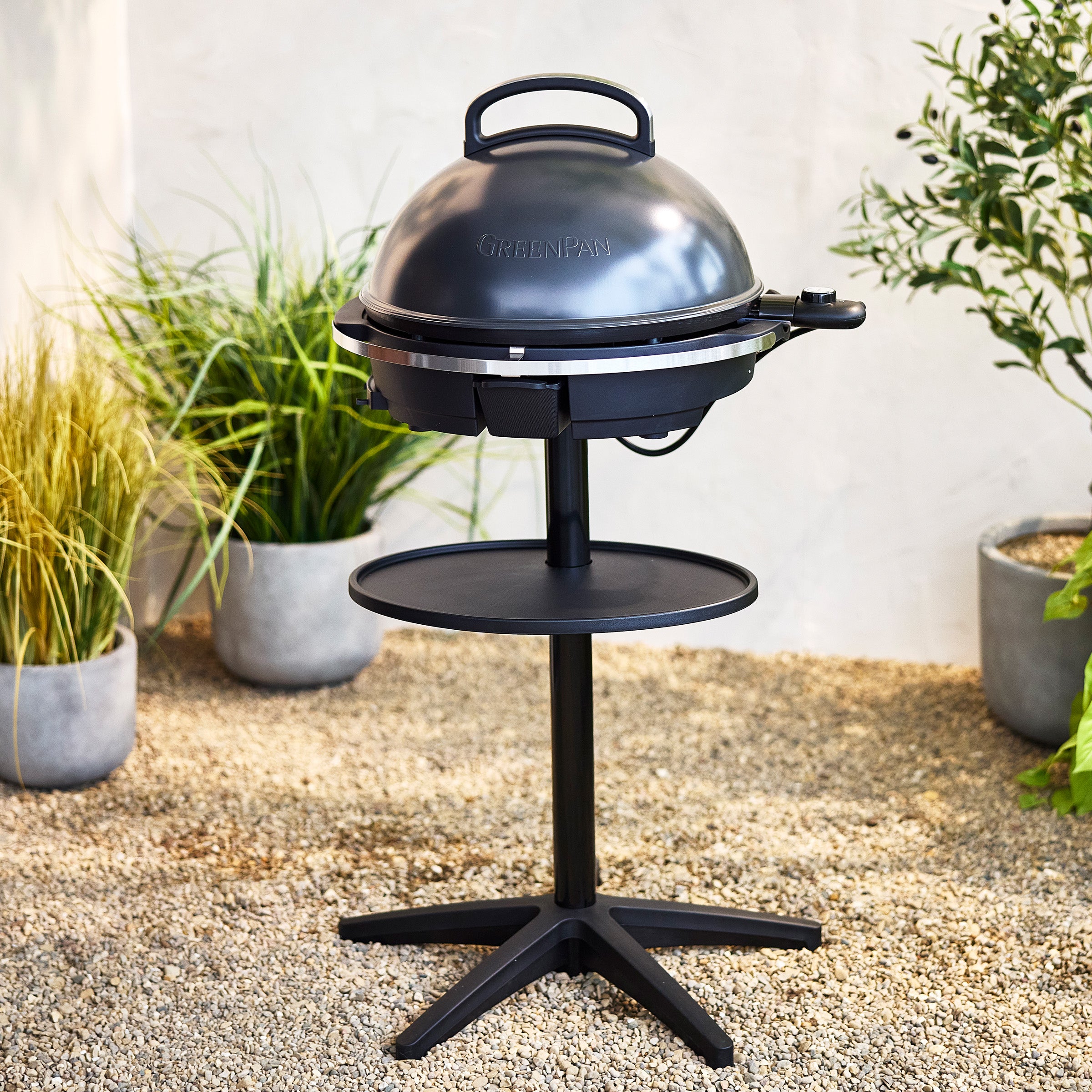 Dark gray portable grill on a stand with plants in the background