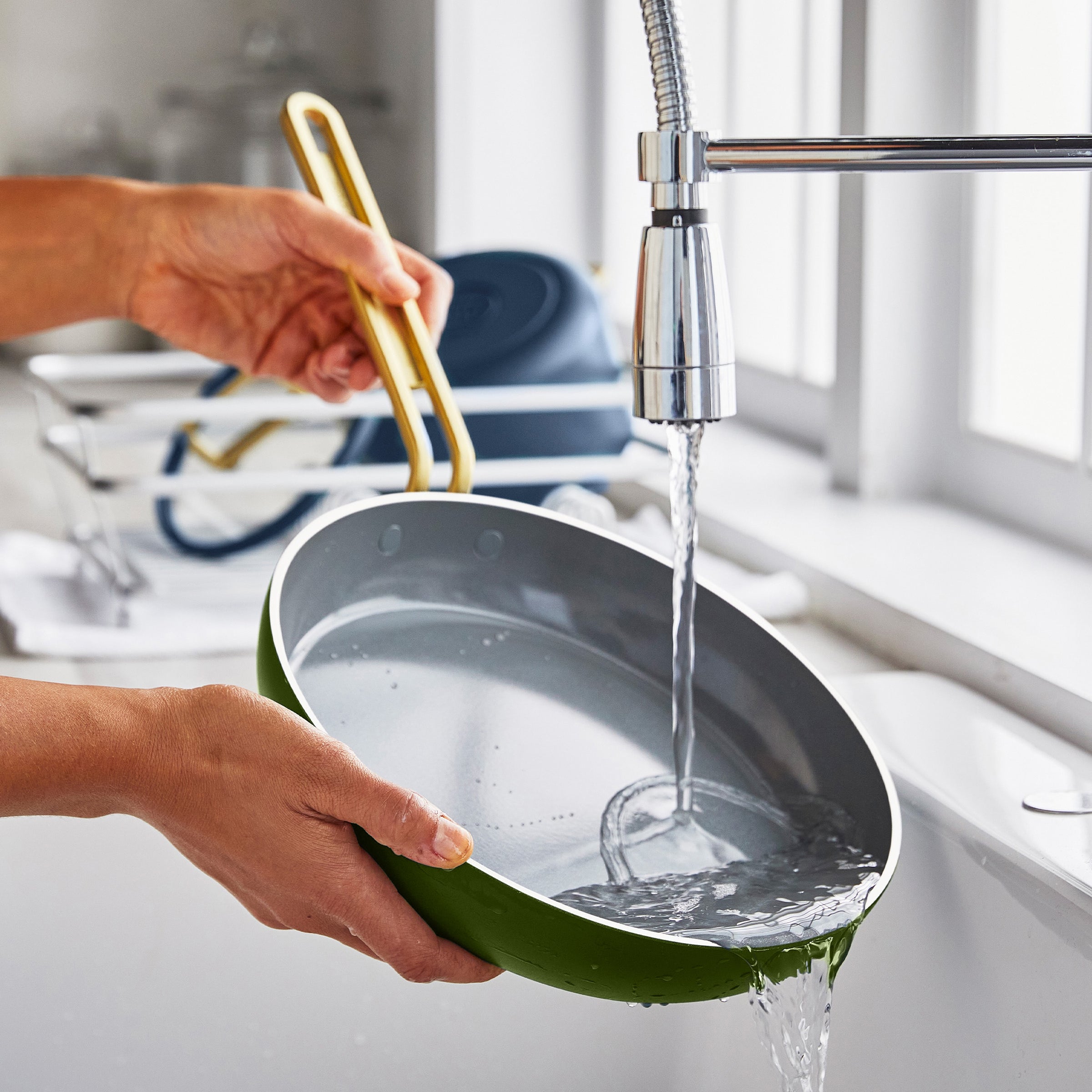 Person washing a green frypan under running water in a kitchen sink.