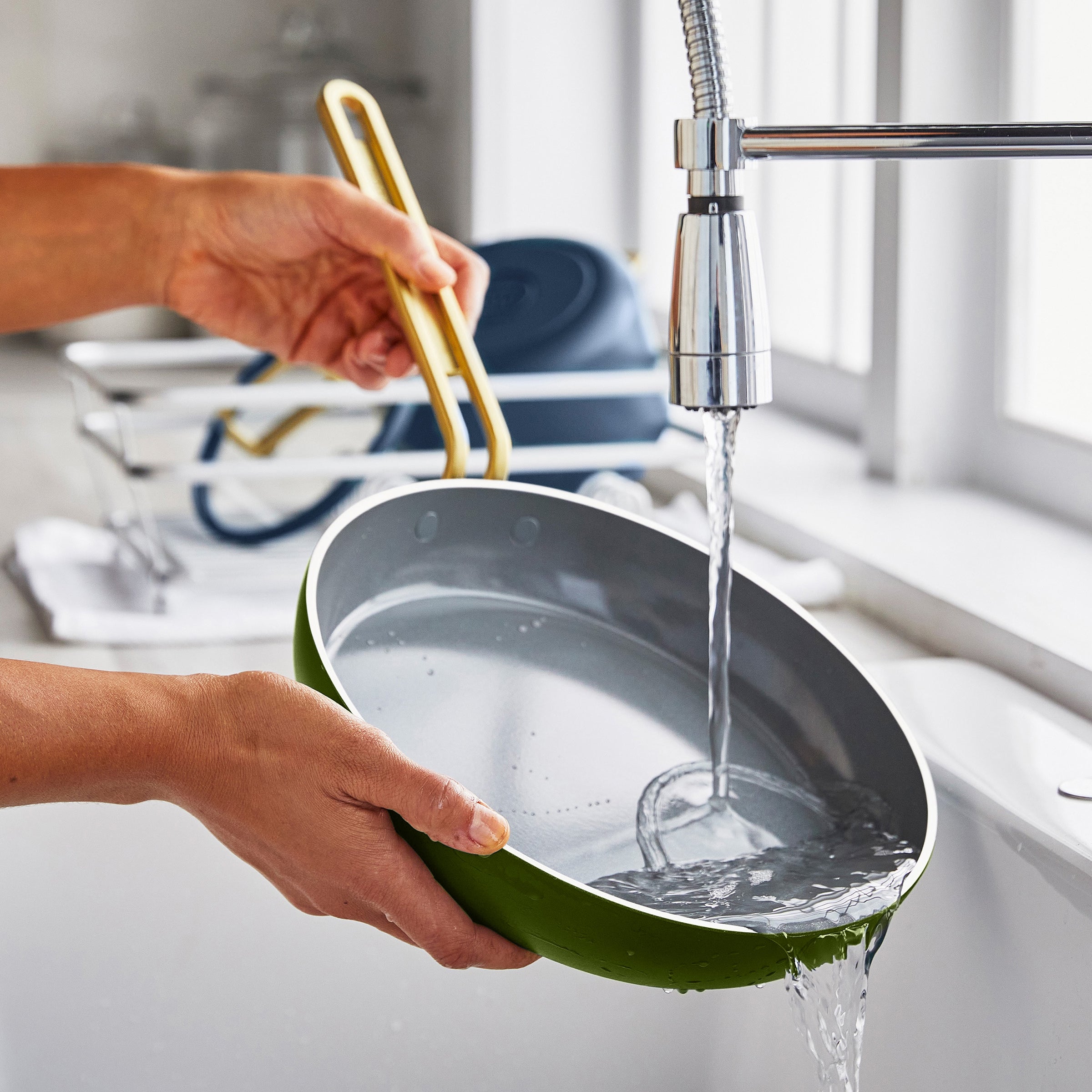 Person washing a green frying pan under running water in a kitchen sink