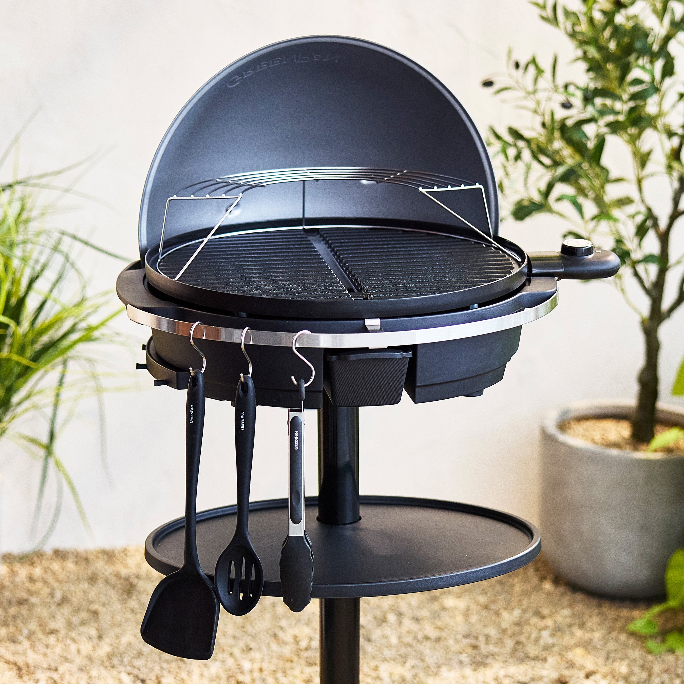 Dark blue portable grill with utensils on a stand outdoors