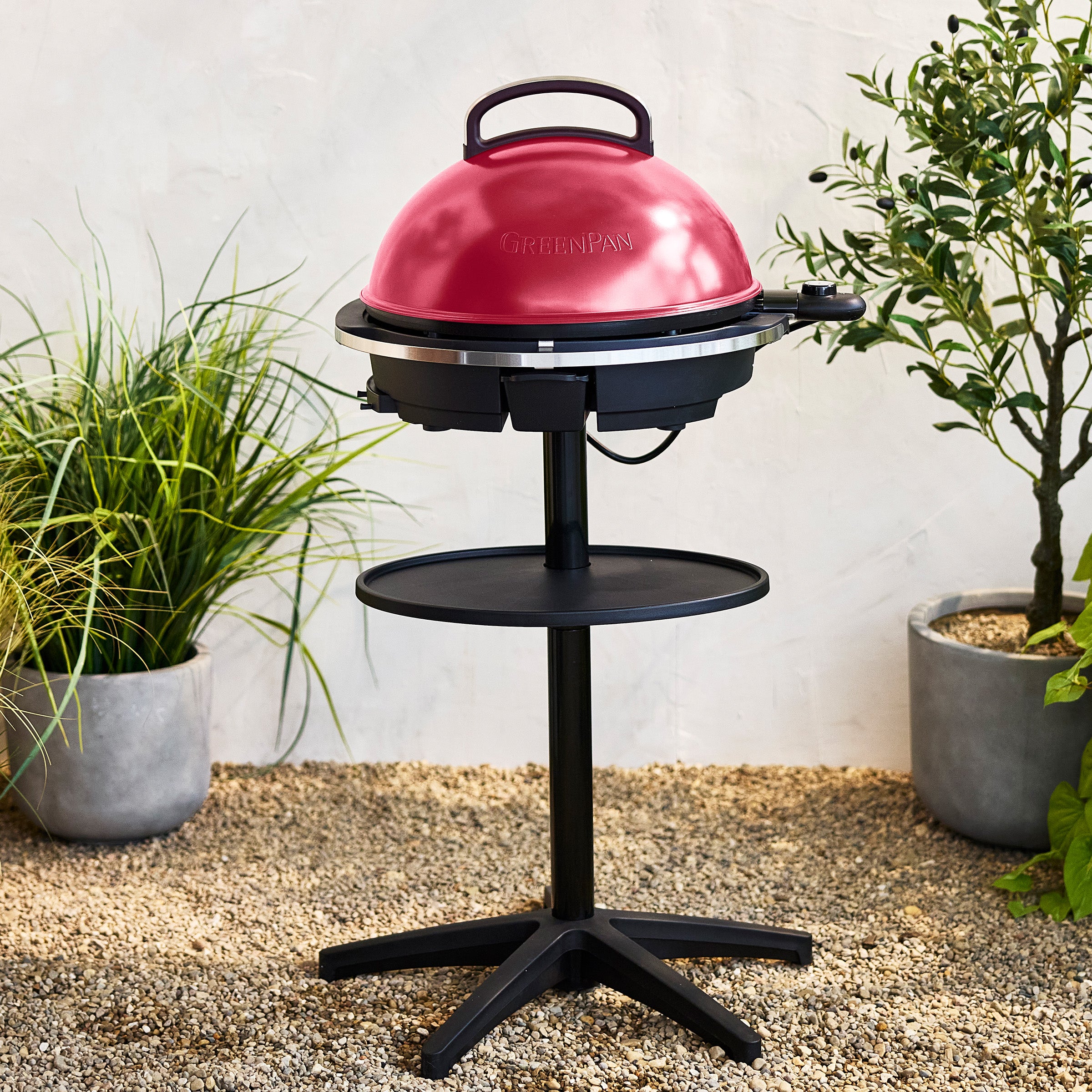 Red portable grill on a stand with plants in the background
