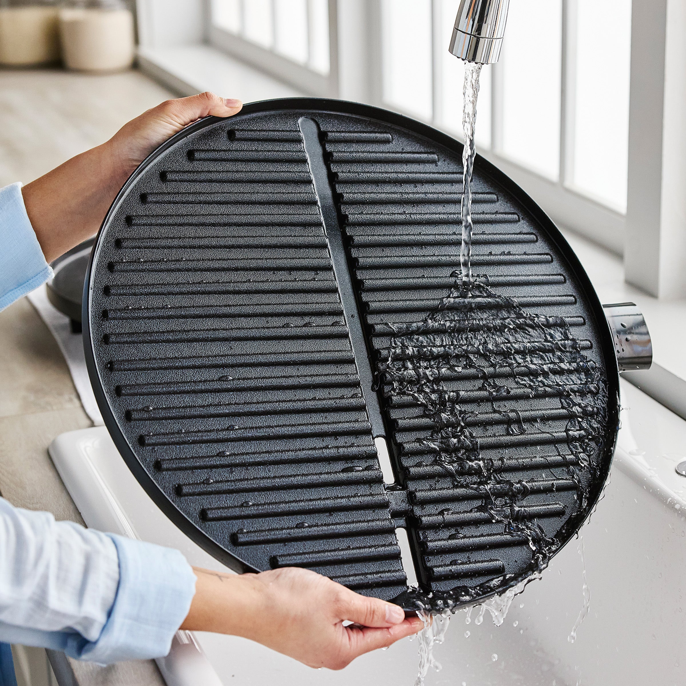 Person washing a grill pan under running water in a kitchen sink