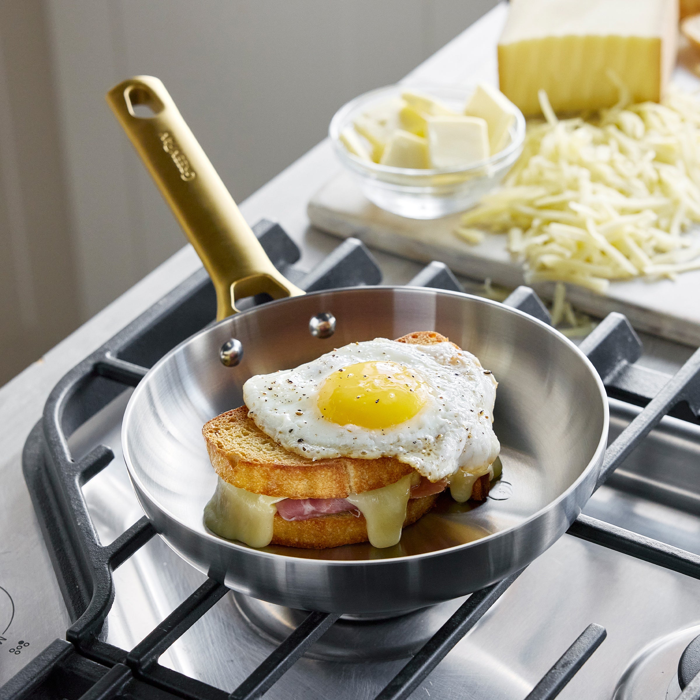 Fried egg on toast in a frying pan on a stove with cheese and butter in the background.