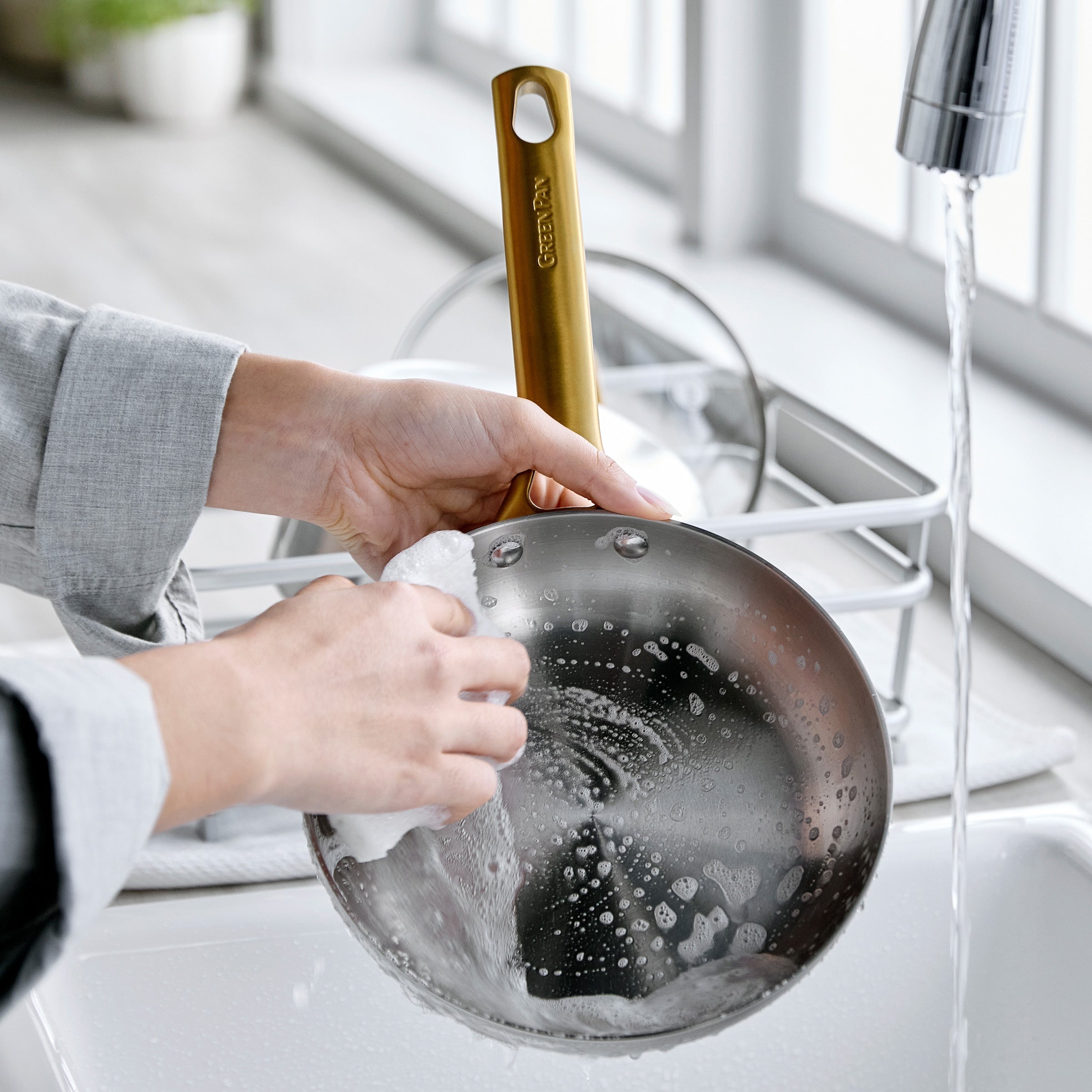 Person washing a frying pan with a sponge in a kitchen sink.
