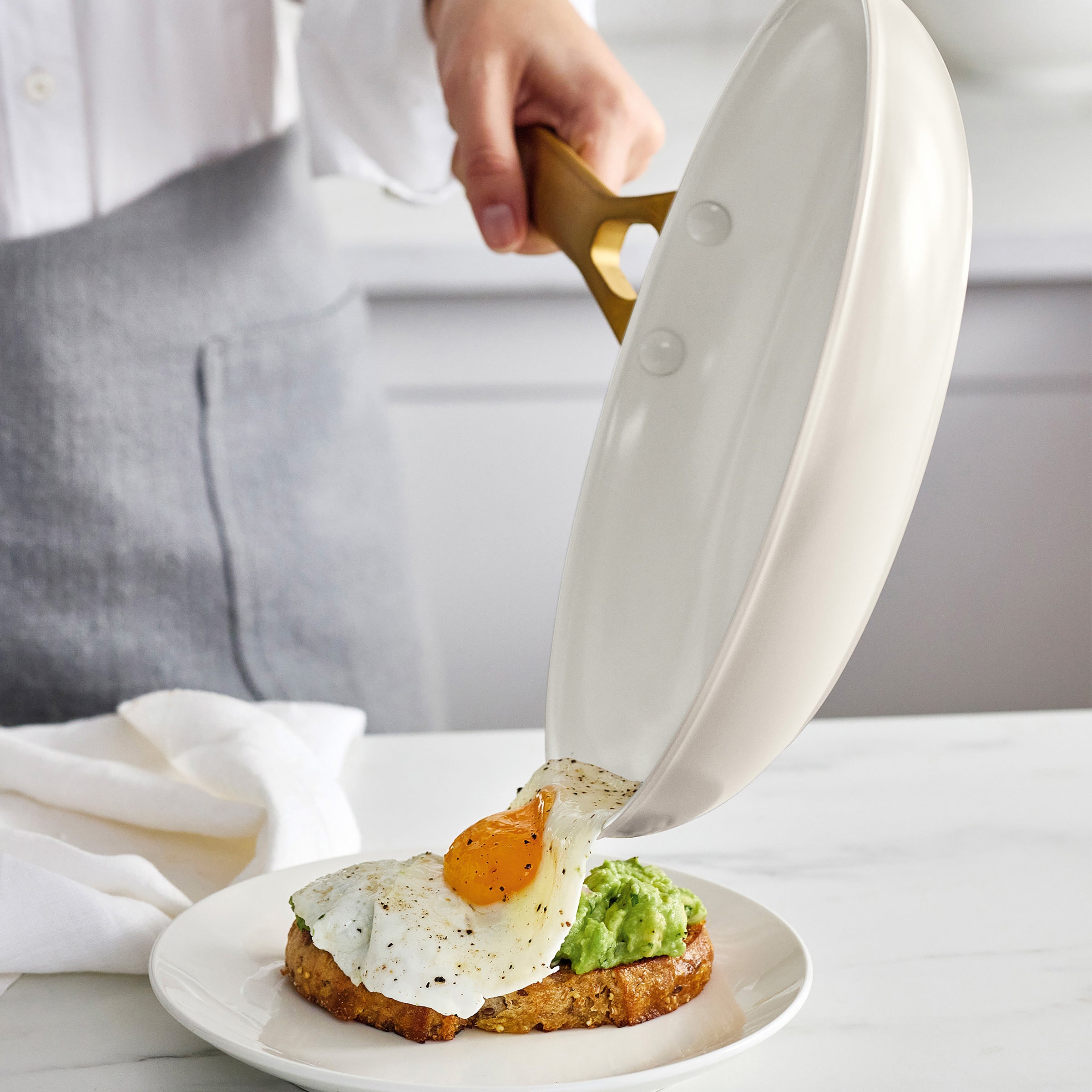 Person pouring an egg onto a plate with avocado toast