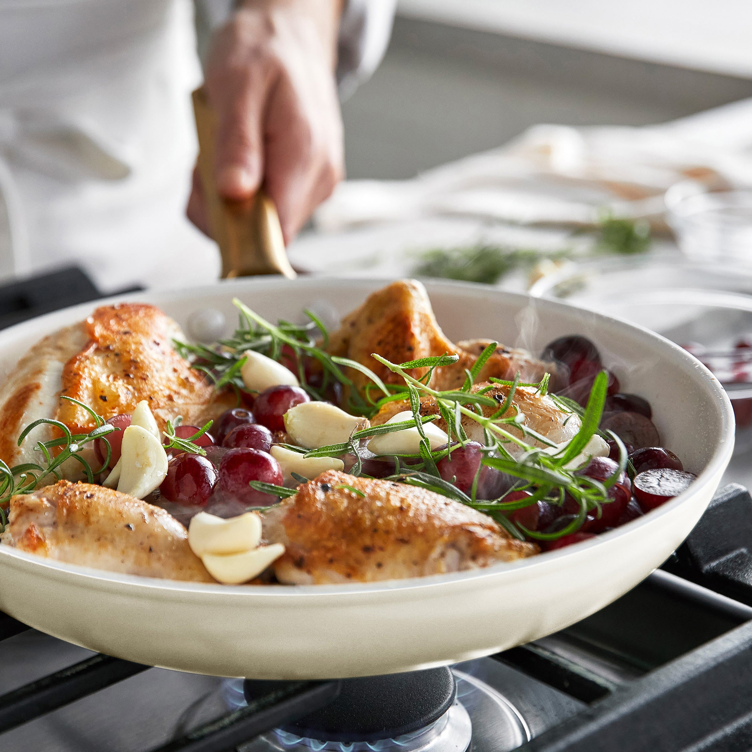 Cream frypan with roasted chicken, grapes, and herbs on a stove