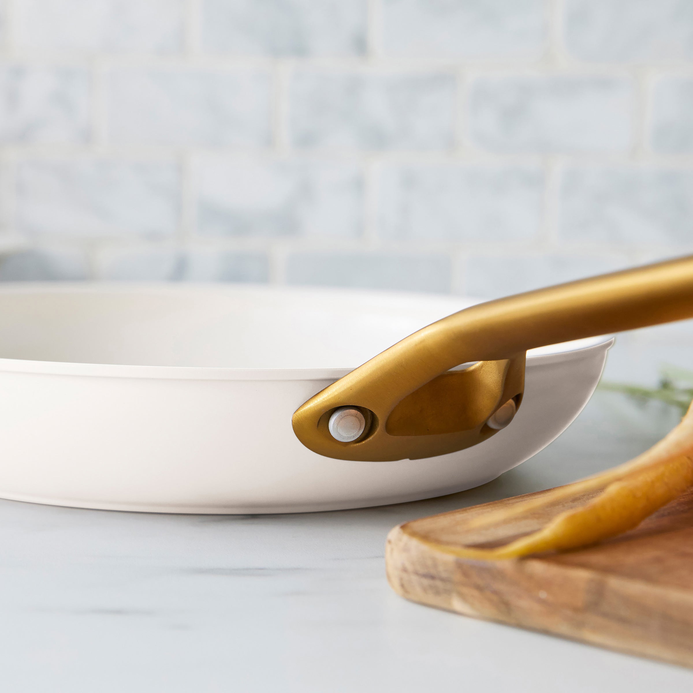 Cream frying pan with a gold handle on a light gray surface.