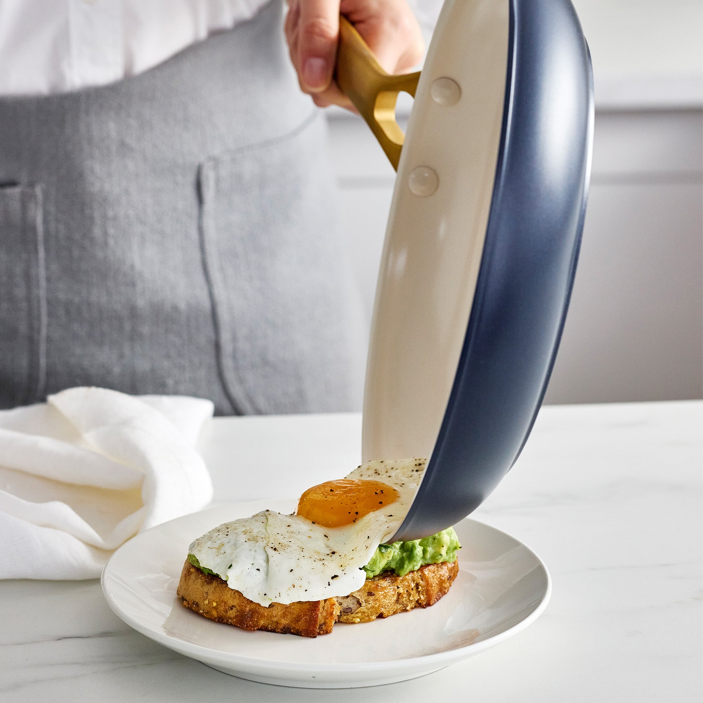 Person using a dark blue frying pan to place an egg on avocado toast