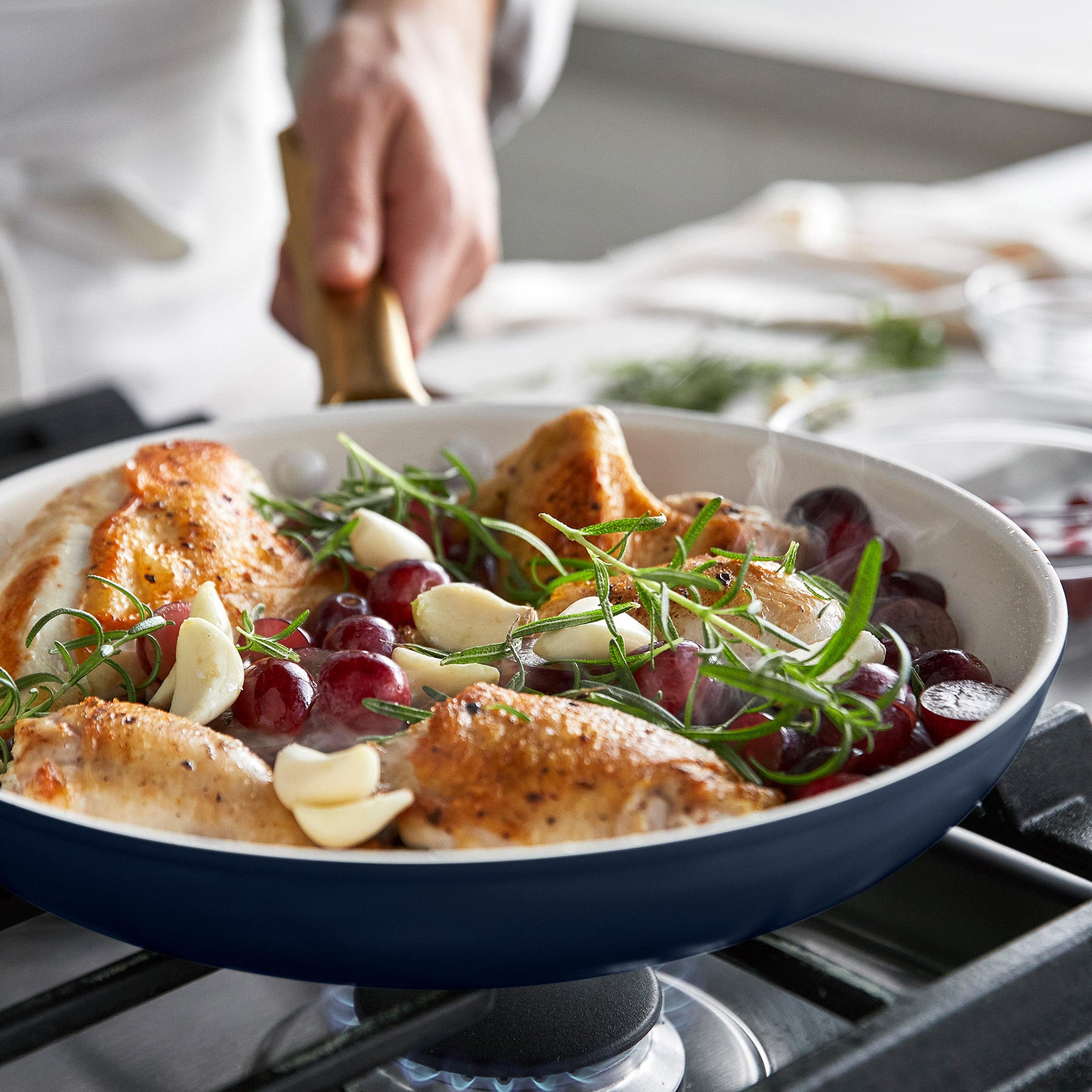 Dark blue frying pan with roasted chicken, grapes, and herbs on a stove