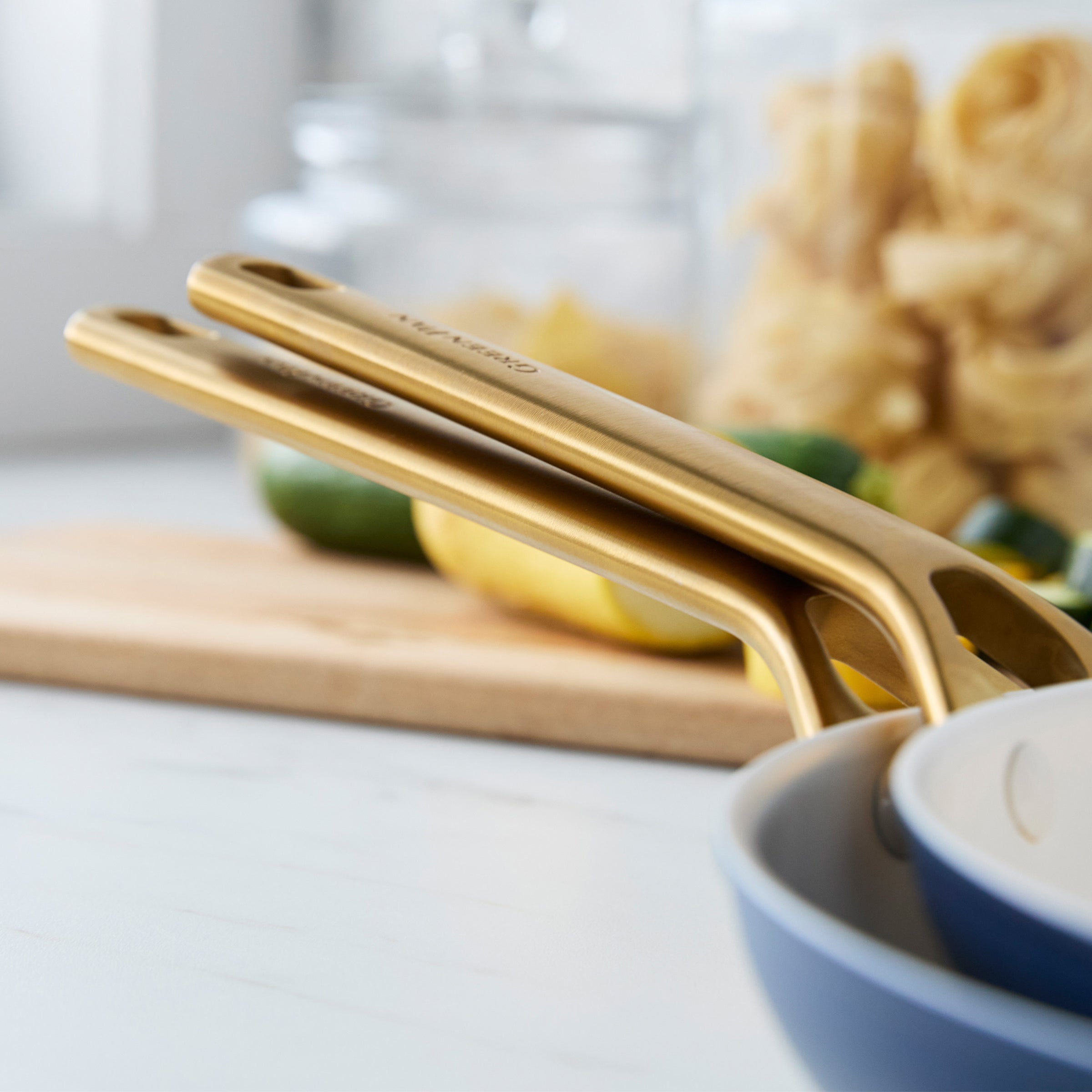 Gold frypan handles on a kitchen counter with a blurred background