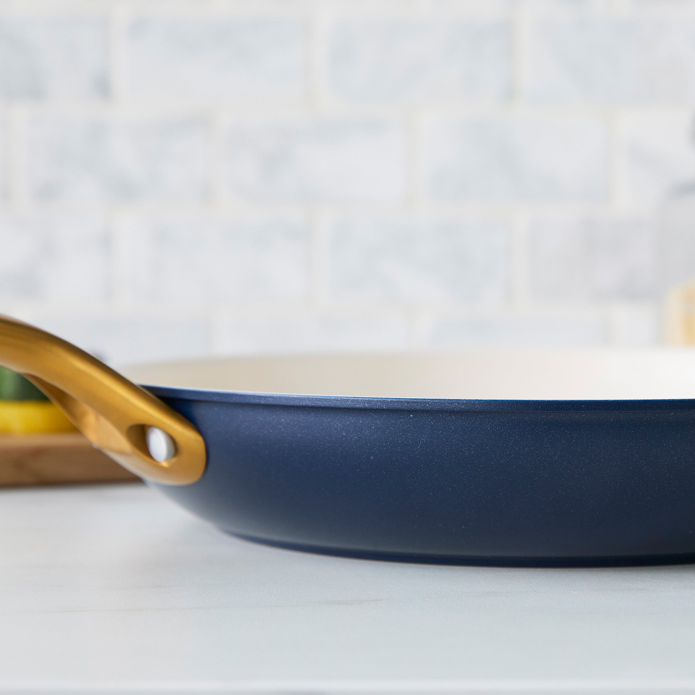 Dark blue frying pan with a gold handle on a white surface
