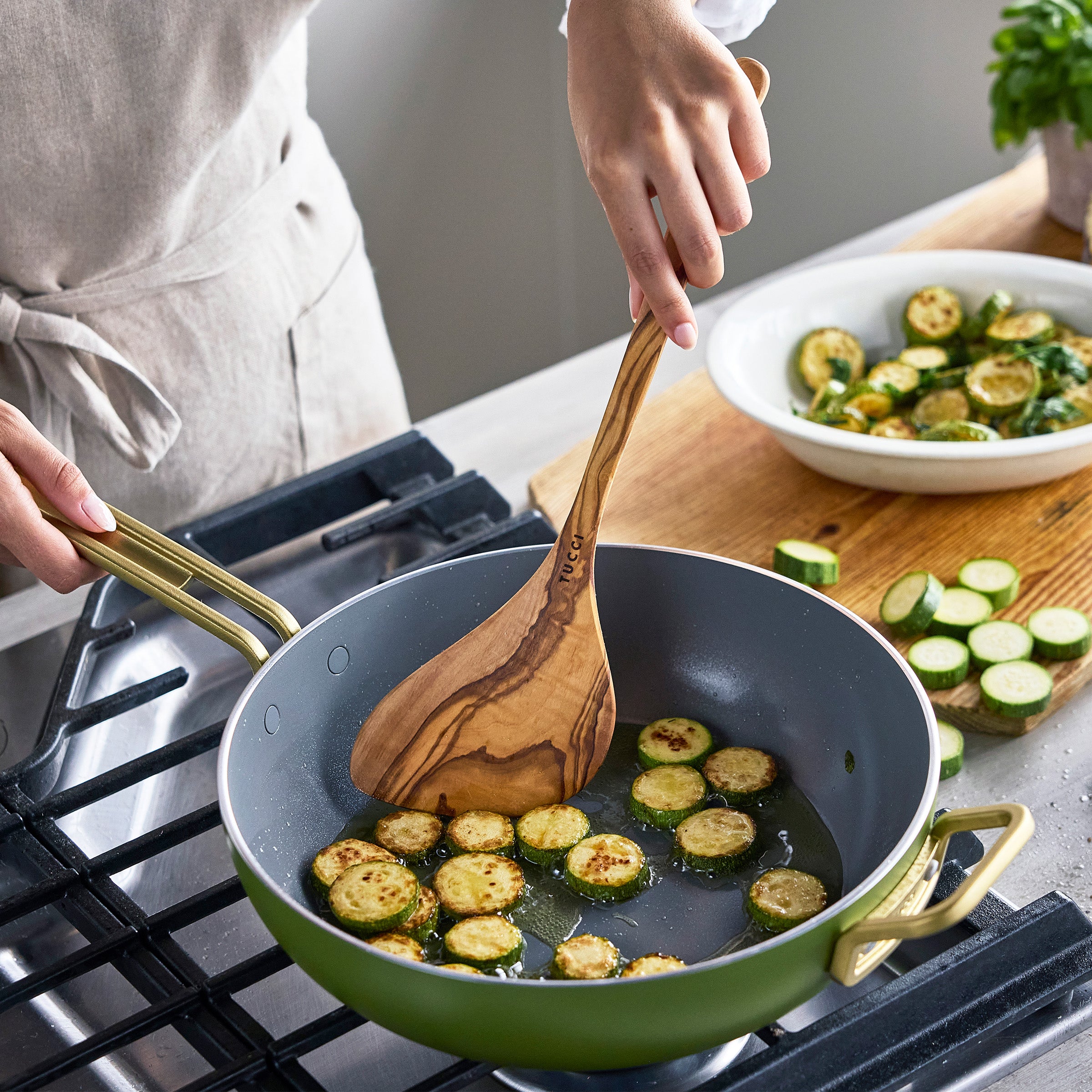 Person cooking zucchini in a green frying pan on a stove
