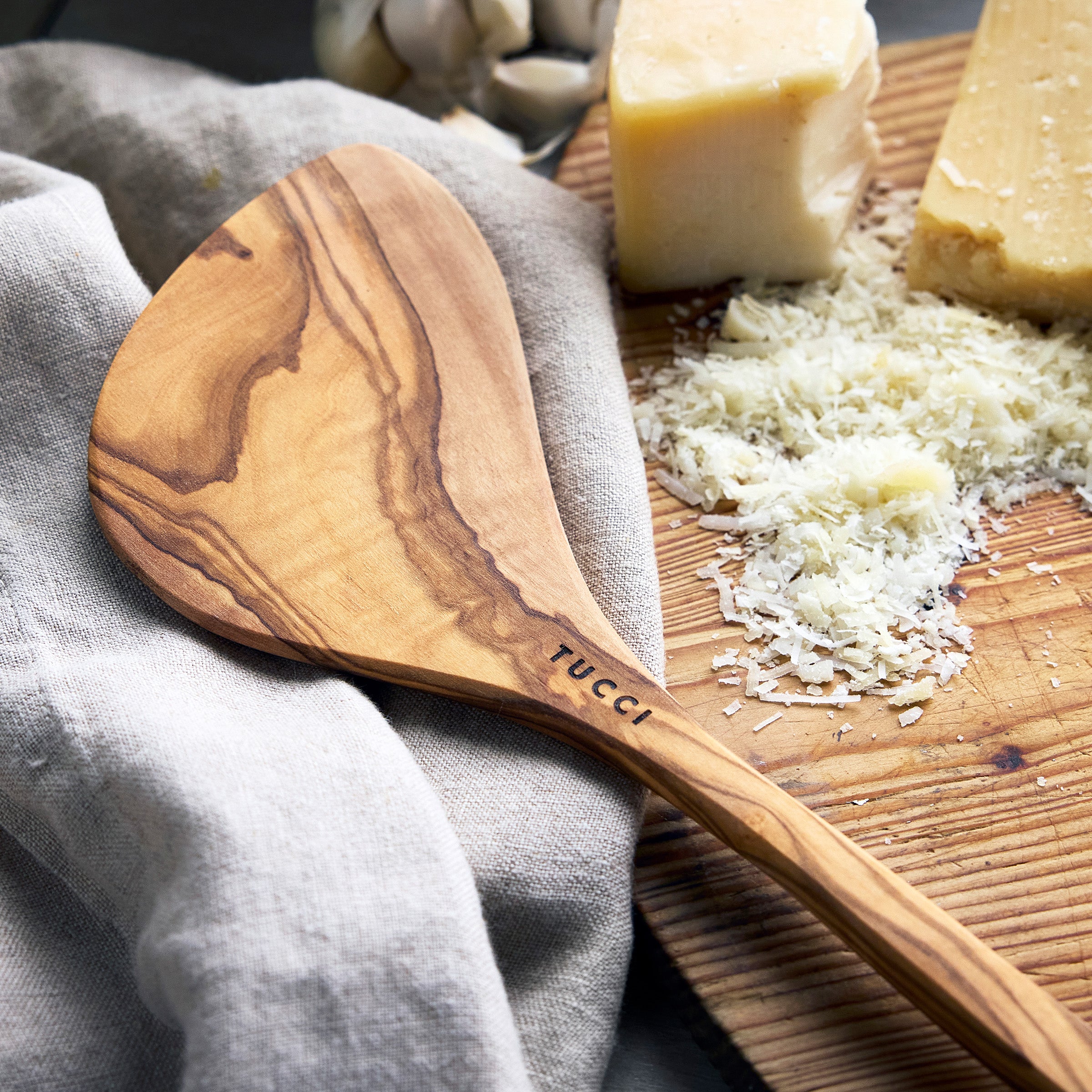 Wooden spoon with 'TUCCI' branding on a wooden board with cheese