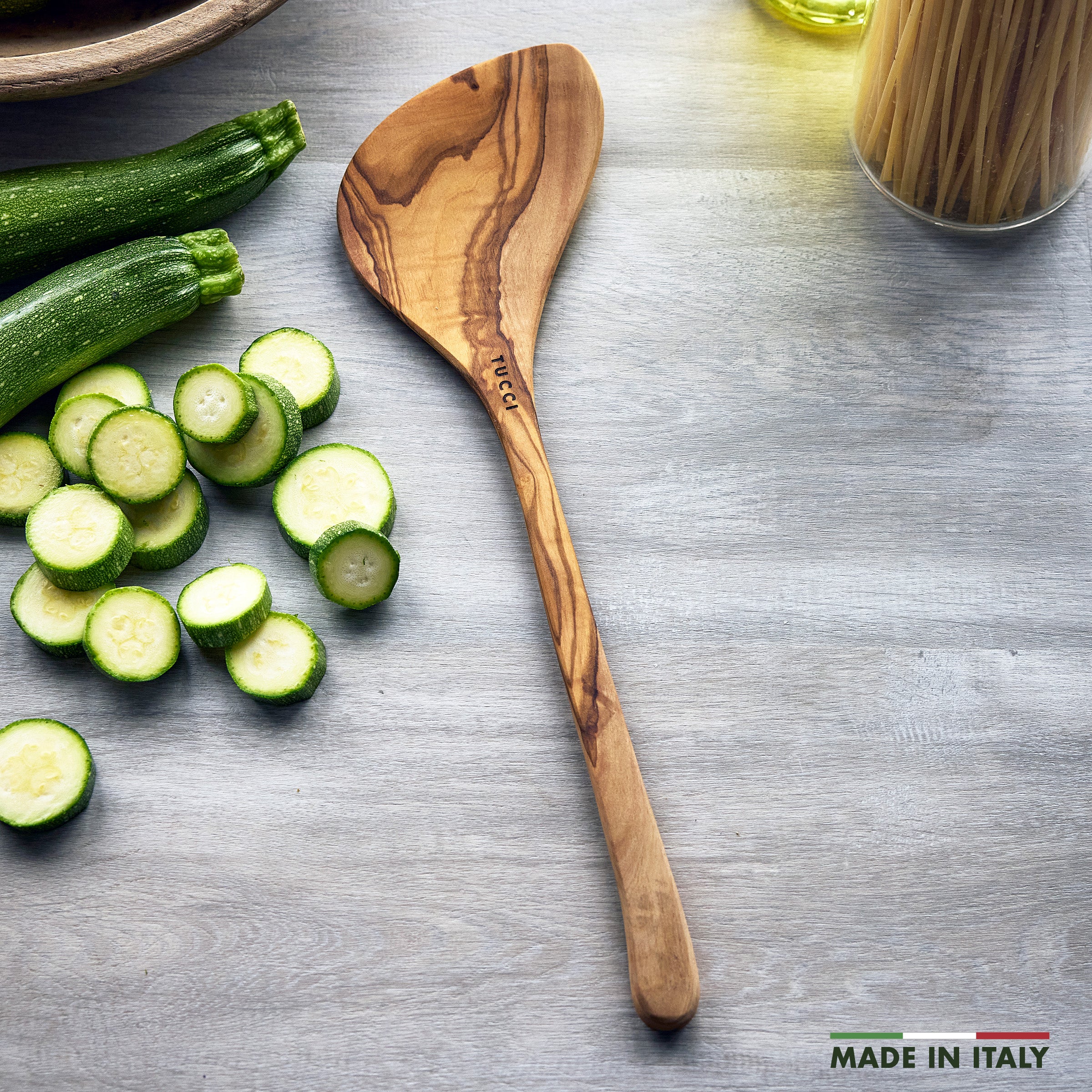 Wooden spoon with sliced zucchini on a gray surface