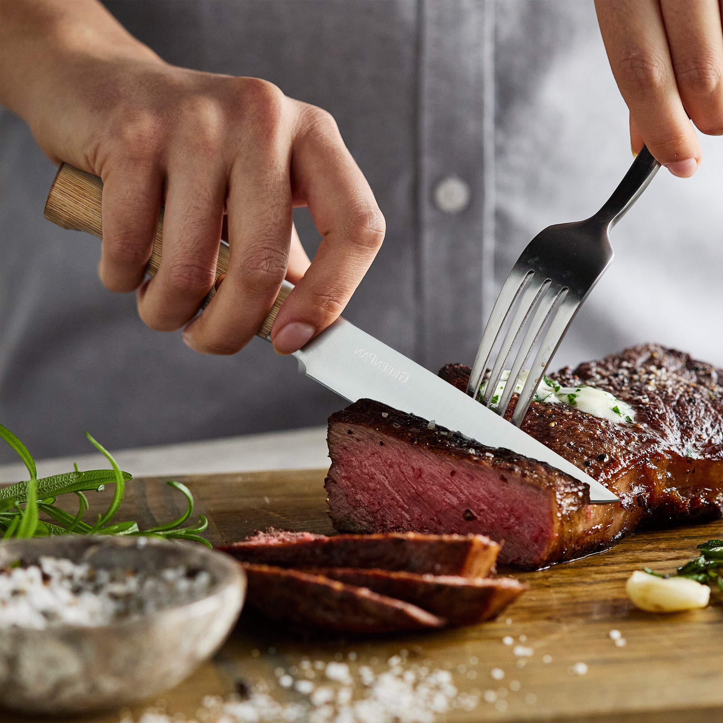 Person cutting a steak with a knife and fork on a wooden cutting board